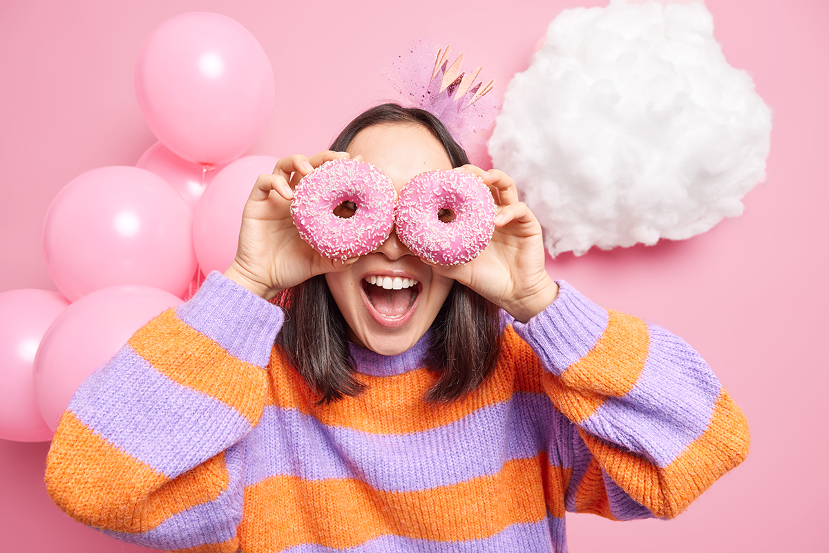 Young woman looking through pink donuts with party balloons in the background