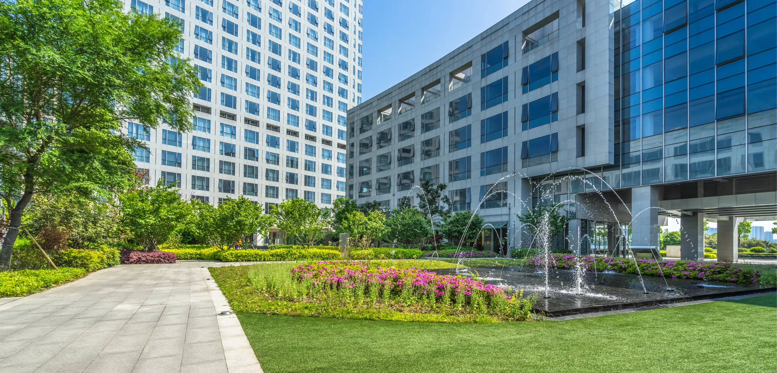 Multi-unit apartment building with a water fountain and garden pathway.